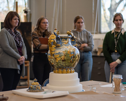 White people stand around a colorful, painted vase resting on foam