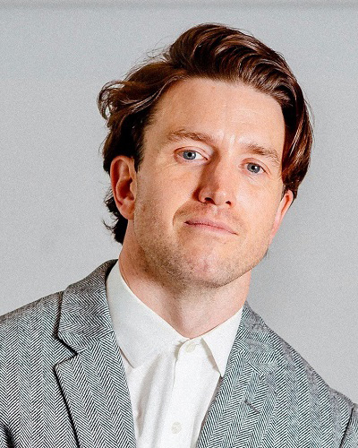 A white man with red hair wearing a gray blazer