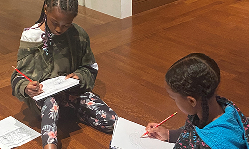 Two young Black visitors sketch in the gallery