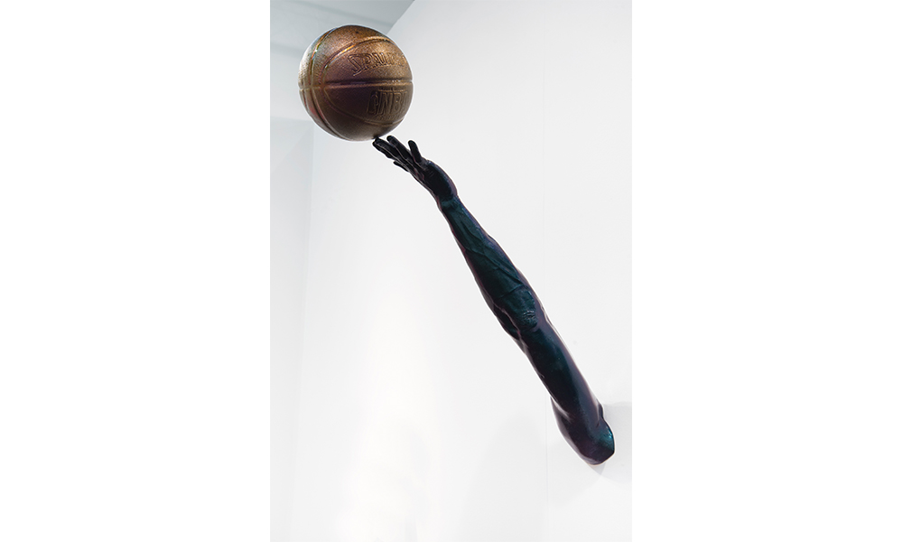 Hank Willis Thomas' Promise, sculpture of an outstretched arm coming out of the wall reaching towards a basketball delicately balanced on the tip of the middle finger