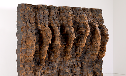sculpture of a wooden wall textured with rough, vertical ridge lines