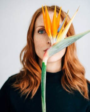 A white woman with red hair posing with an orange flower