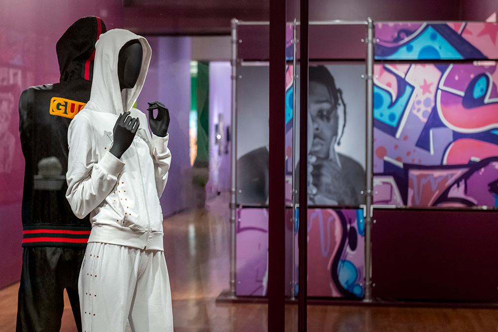 Two mannequins wearing streetwear in front of a wall with purple and blue graffiti