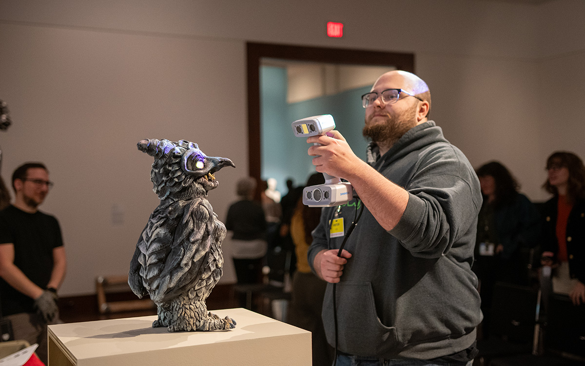 A white man holds an IR scanner and points it at a 3D artwork