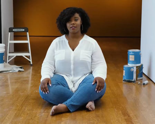 A Black woman sits cross-legged in a gallery