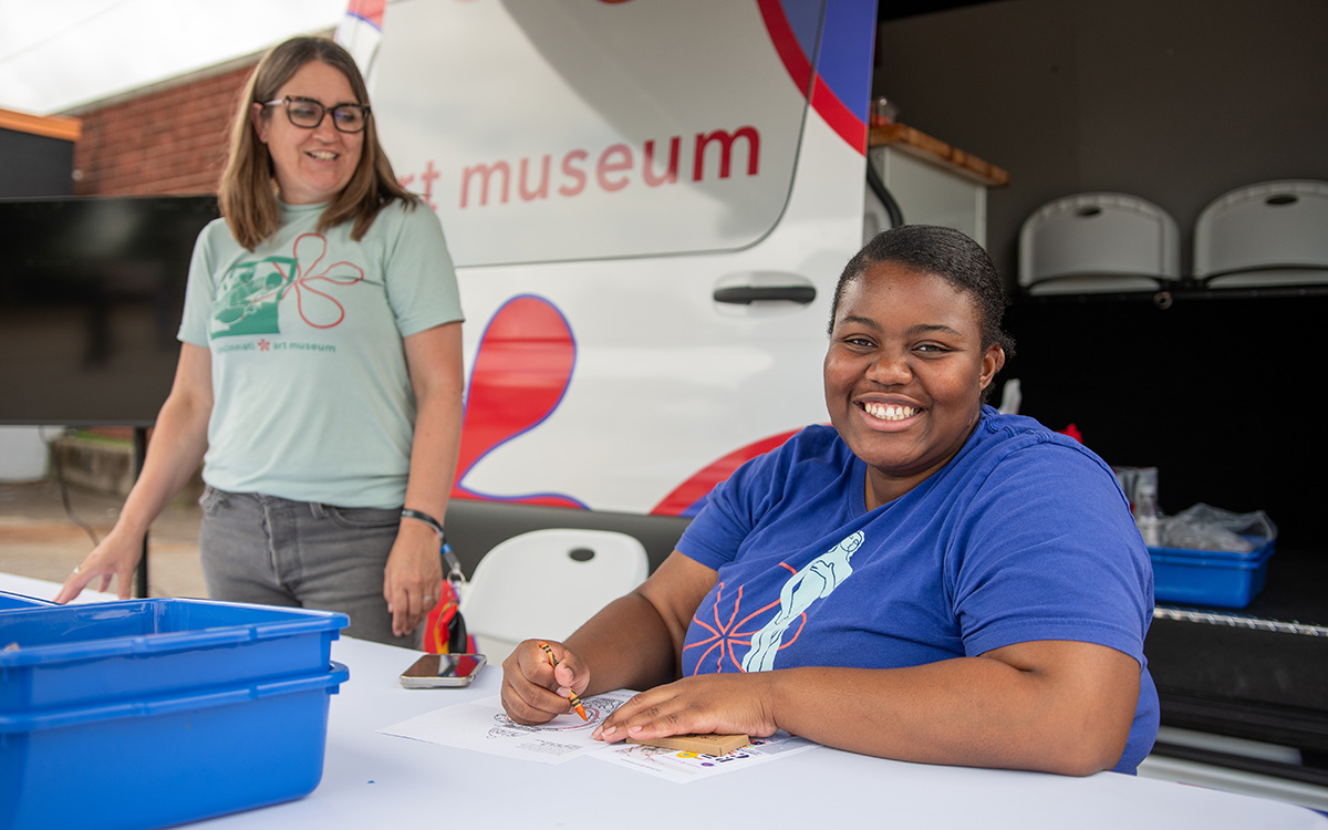 A Black woman and white woman smile at a table outside the CAM Cruiser