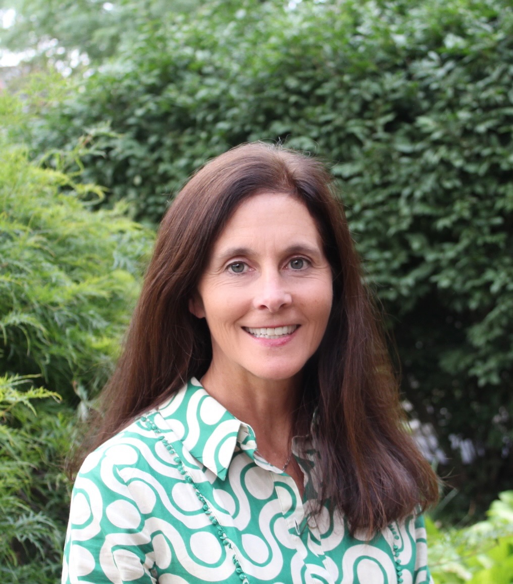 A smiling white woman with brown hair wearing a swirly green and white top.