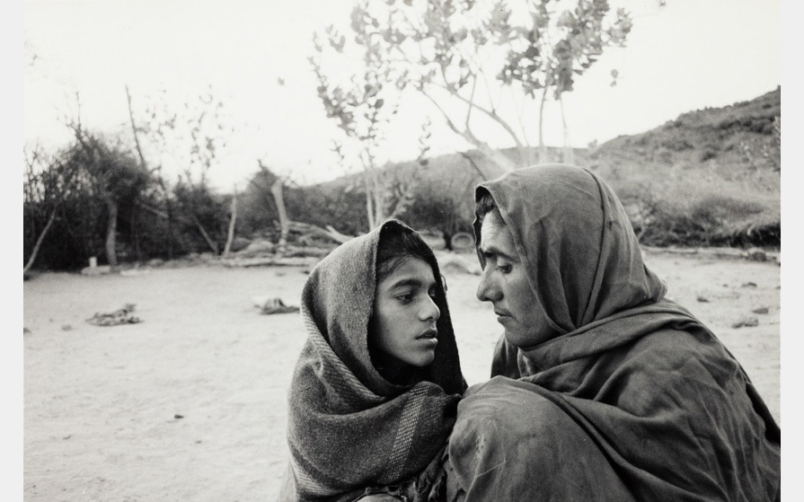 Two people wrapped in fabric look closely into each other’s faces